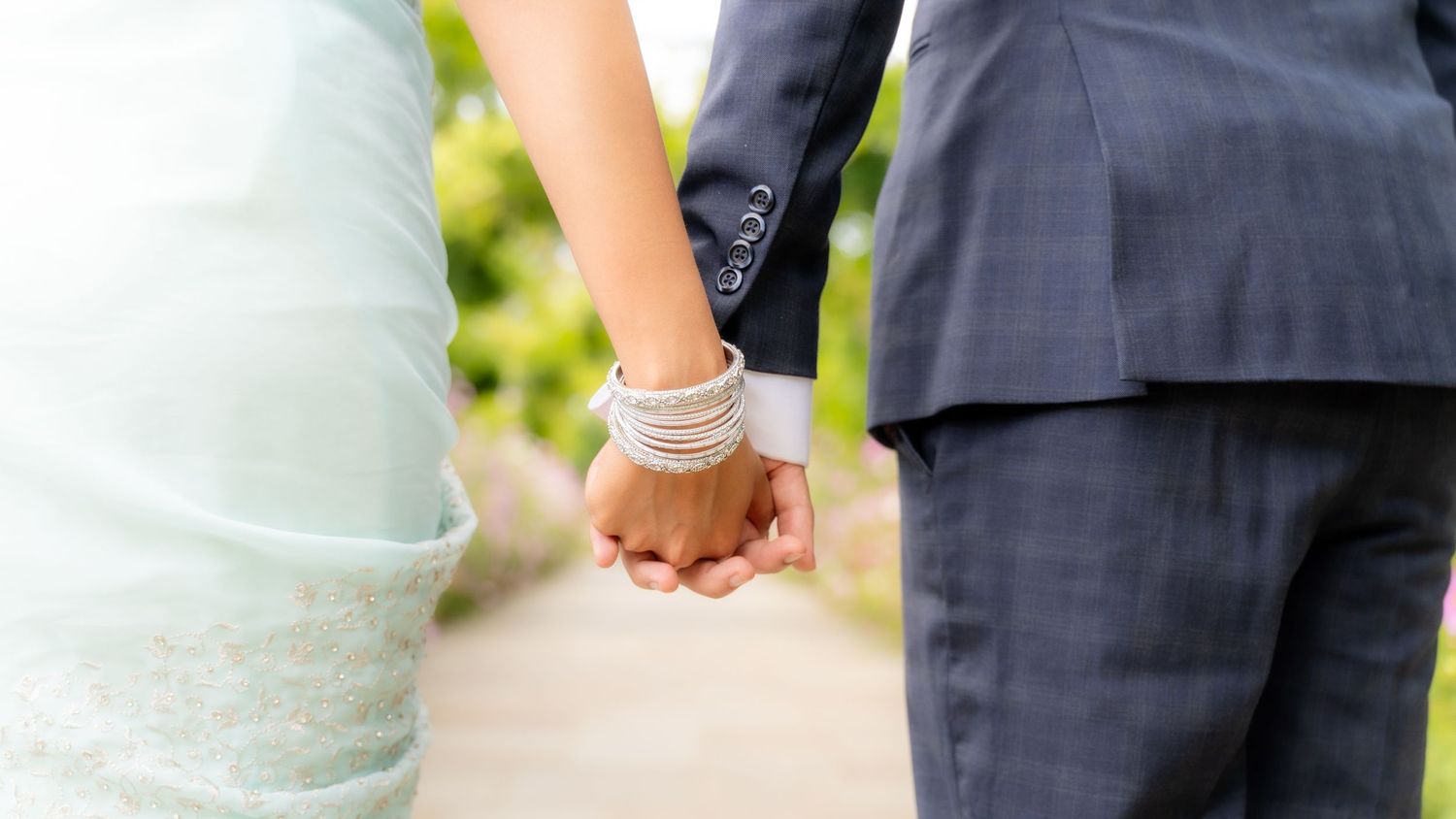 Couple holding hands with white ribbon binding at outdoor wedding ceremony.