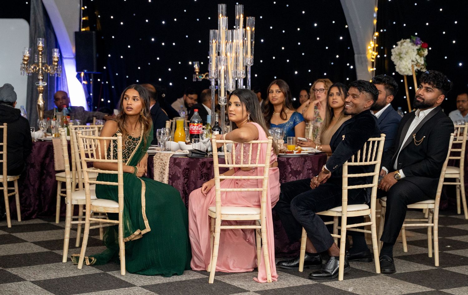 Guests in traditional Indian attire seated at elegant wedding reception with candlelit centerpieces.