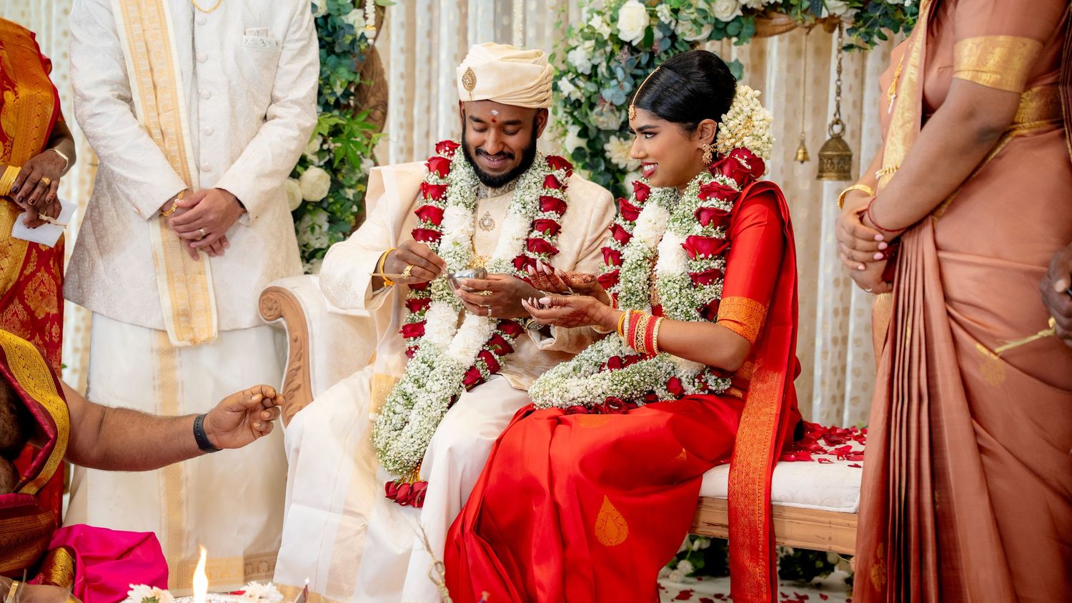 Groom places ring on brides hand during traditional South Indian Hindu wedding ritual with floral decorations.
