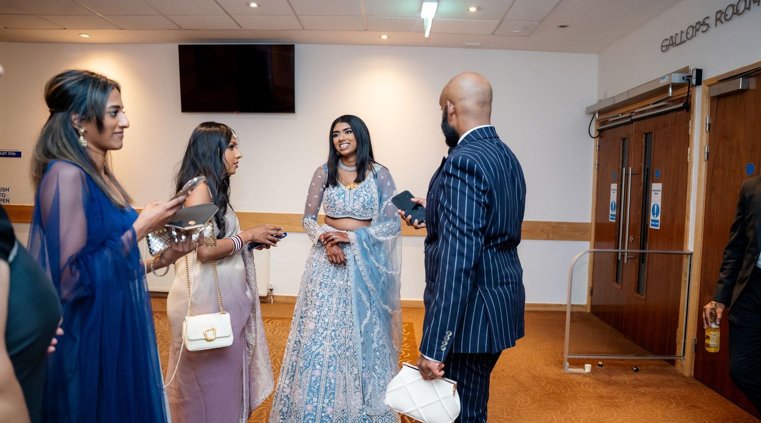 Guests in formal Indian attire converse in a venue hallway at a wedding reception.