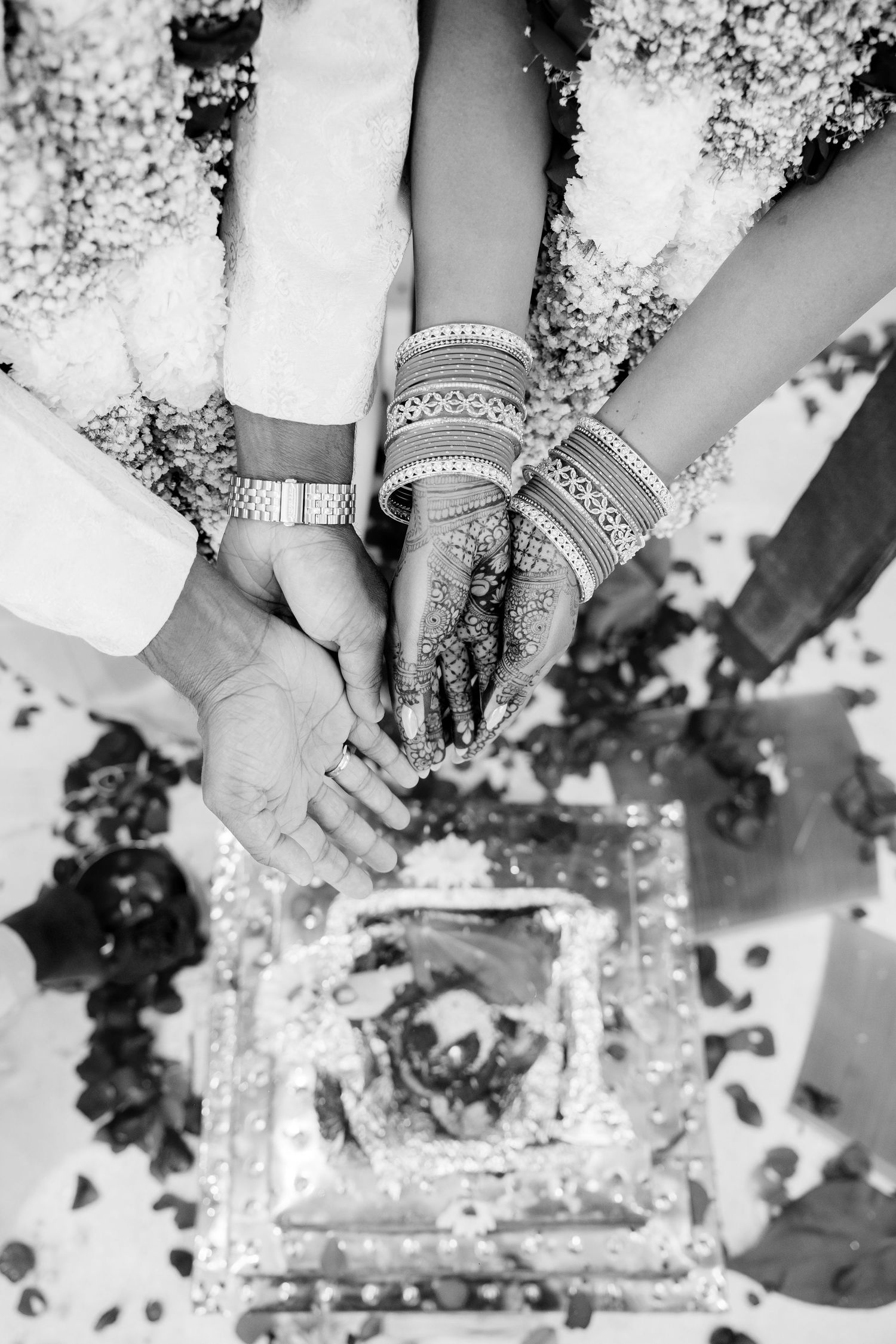 Black and white close-up of bride and groom hands with henna mehndi and bangles during Hindu wedding ritual.