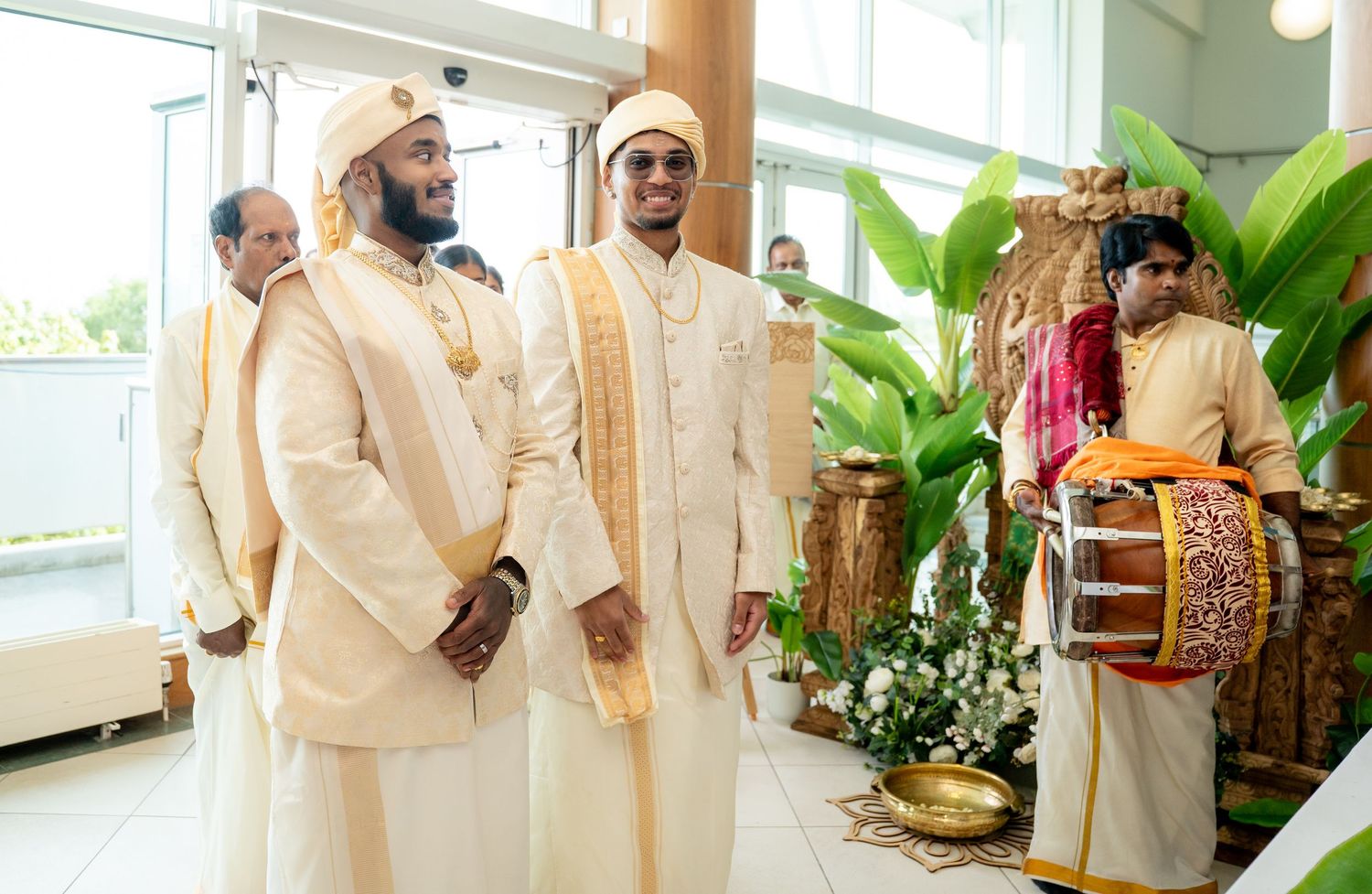 Two grooms in matching cream sherwanis and golden turbans standing together at a traditional Hindu wedding ceremony.