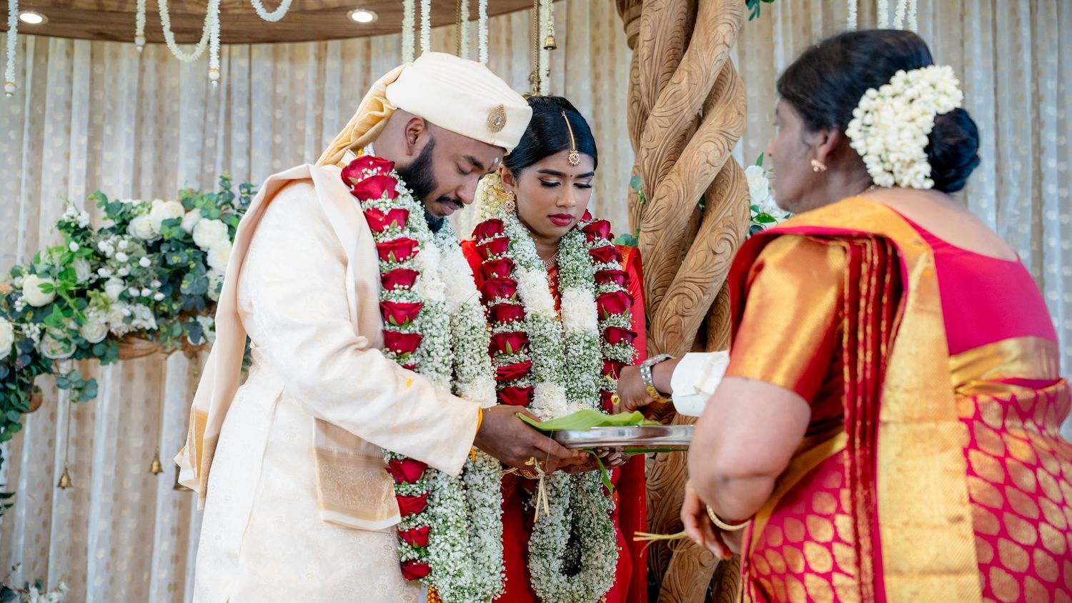 Bride and groom receive blessings during colorful South Indian wedding ceremony with floral garlands.