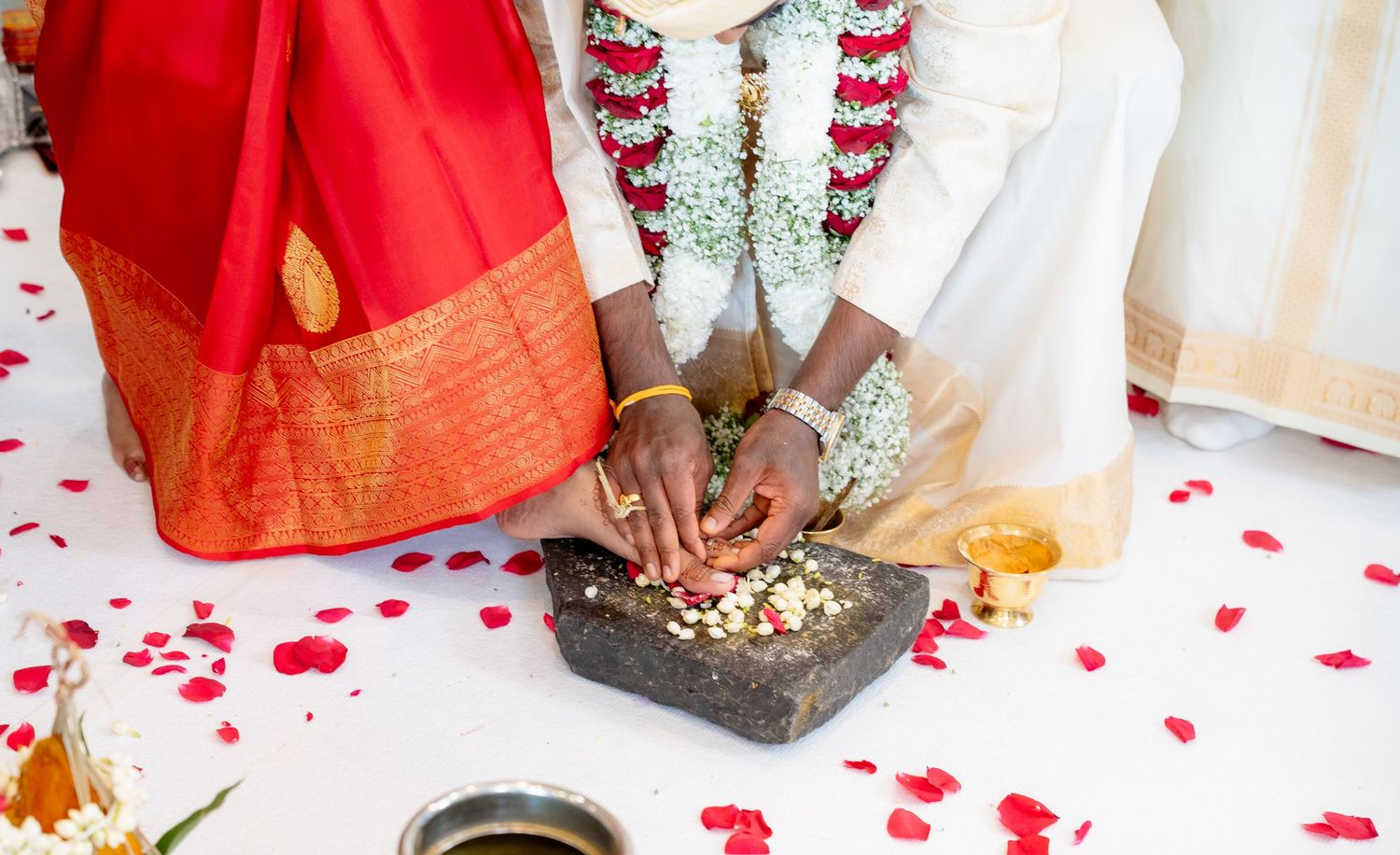 Hindu wedding couple performing traditional ritual with flower offerings surrounded by rose petals.