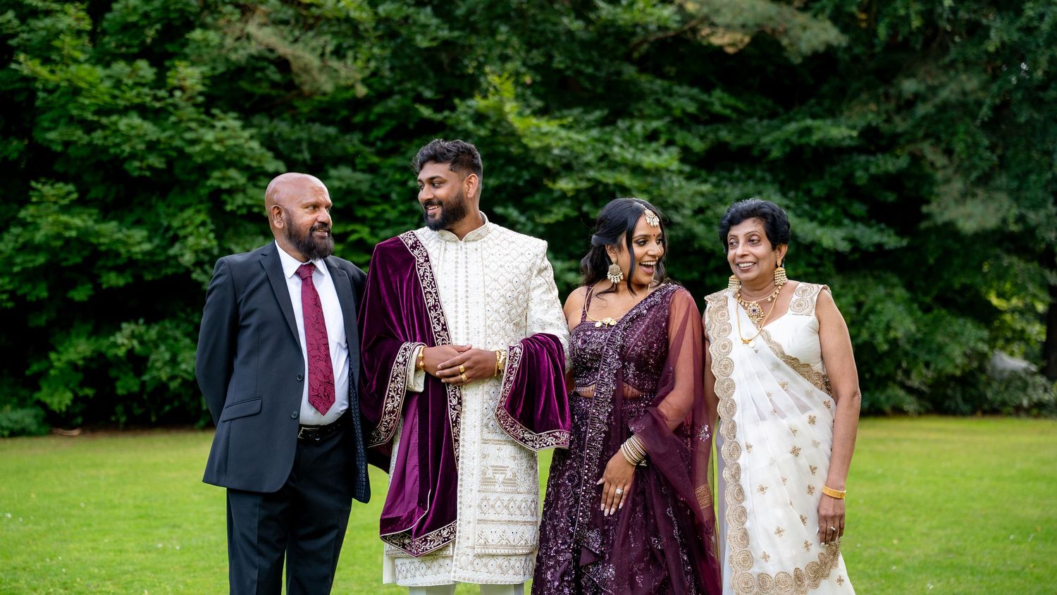 South Asian wedding family portrait with groom in sherwani and guests in traditional attire outdoors.