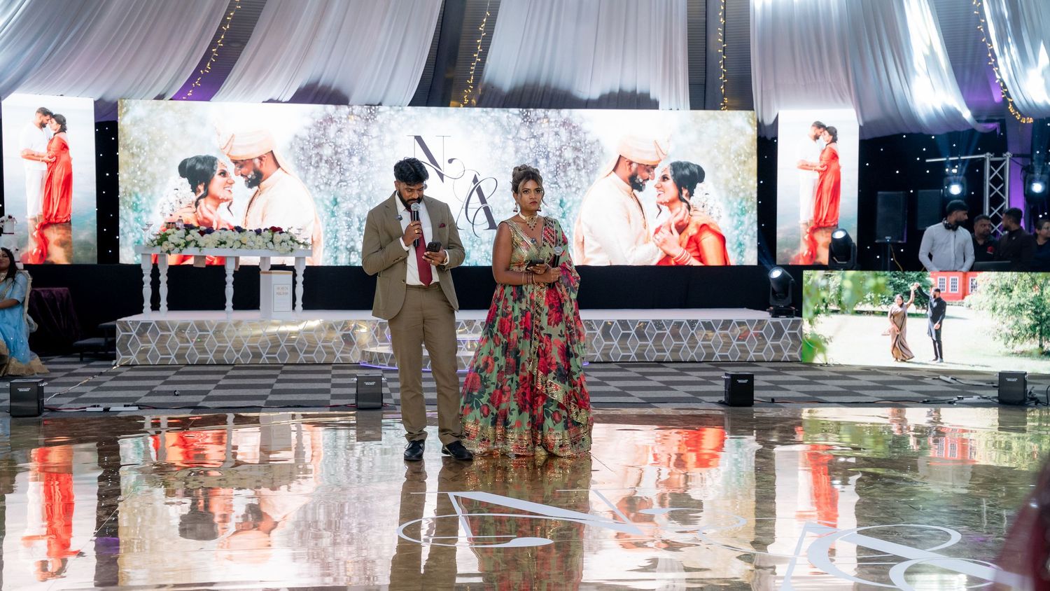 Bride and groom in traditional Indian wedding outfits standing on reflective dance floor at reception.