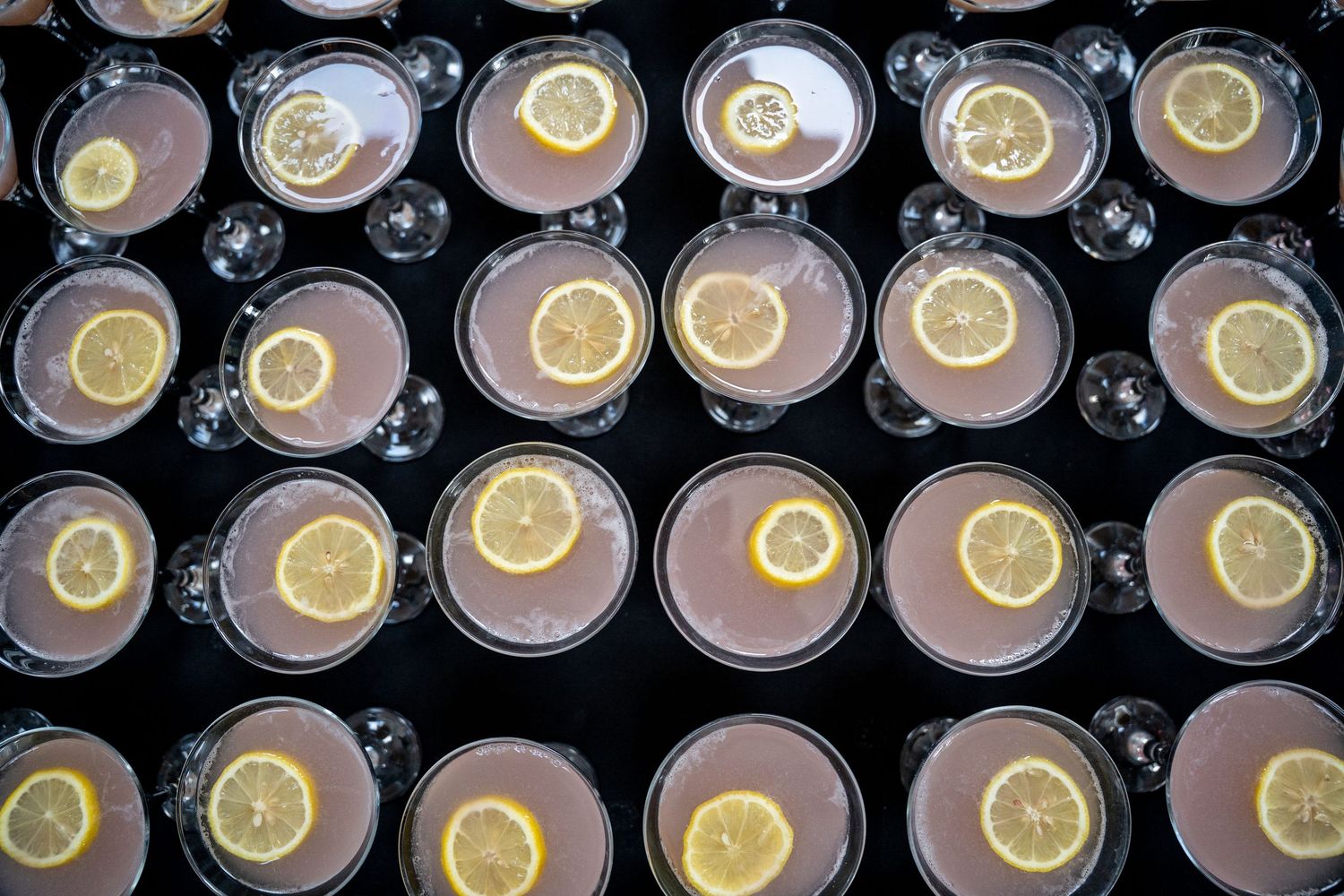 Overhead view of rows of pink lemonade cocktails garnished with lemon slices in clear glasses.