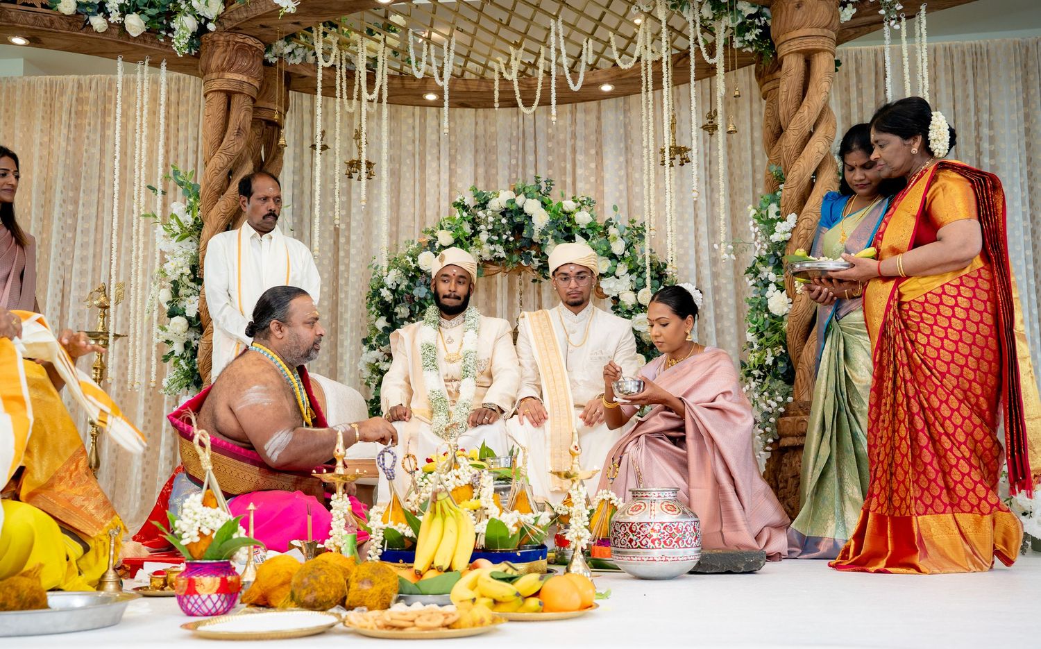 Traditional South Indian wedding ceremony with priest, couple, and family gathered under floral mandap.