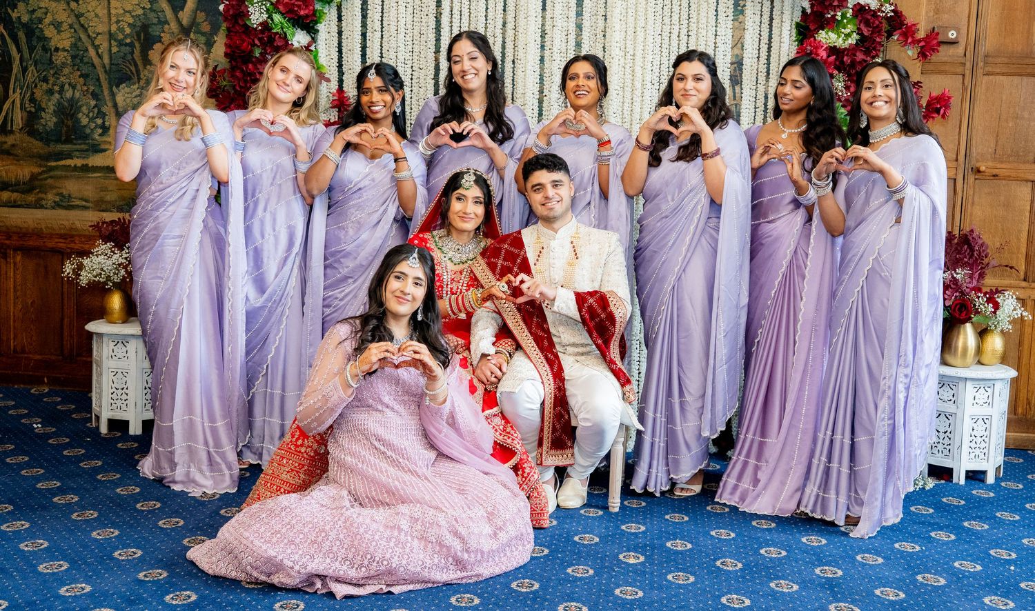 Wedding party making heart gestures with bridesmaids in matching lavender sarees.