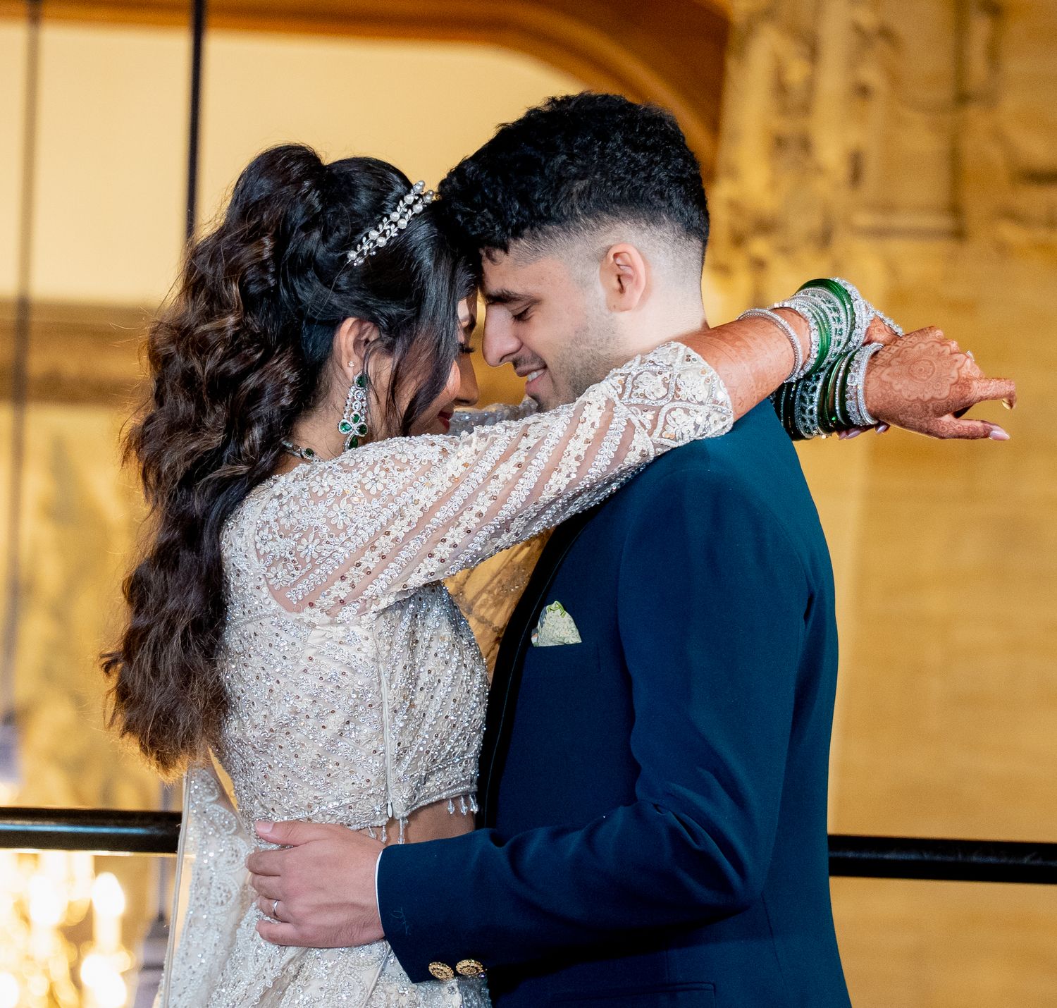 South Asian couple in wedding attire share romantic embrace, bride wearing white lehenga and green bangles.