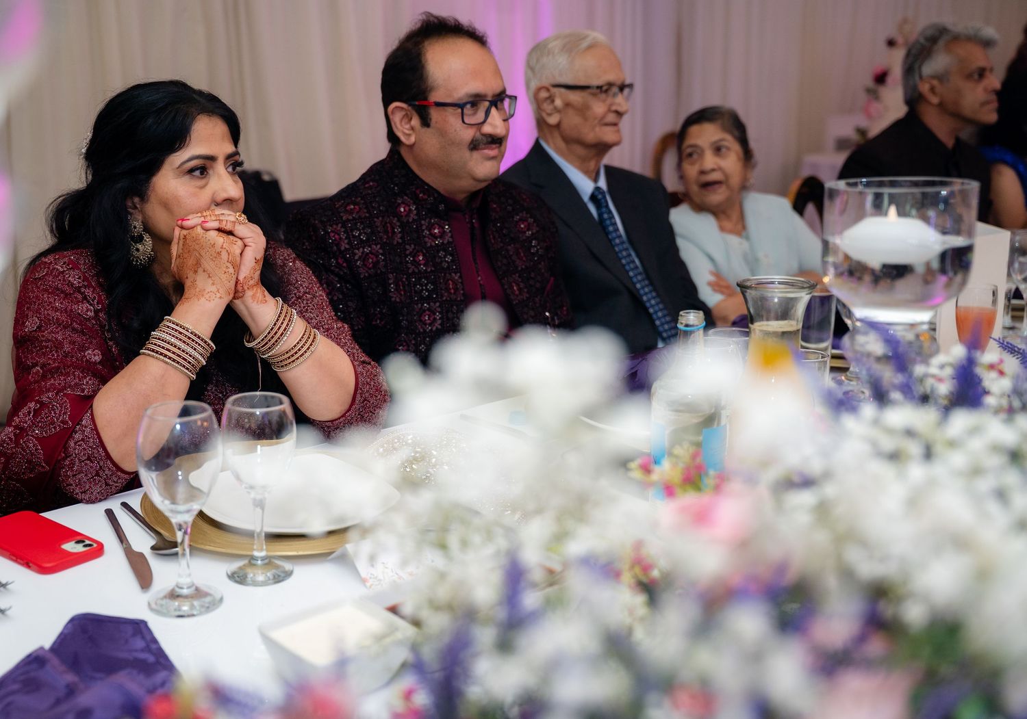 Guests in formal attire seated at a decorated banquet table with floral centerpieces at an Indian wedding reception.