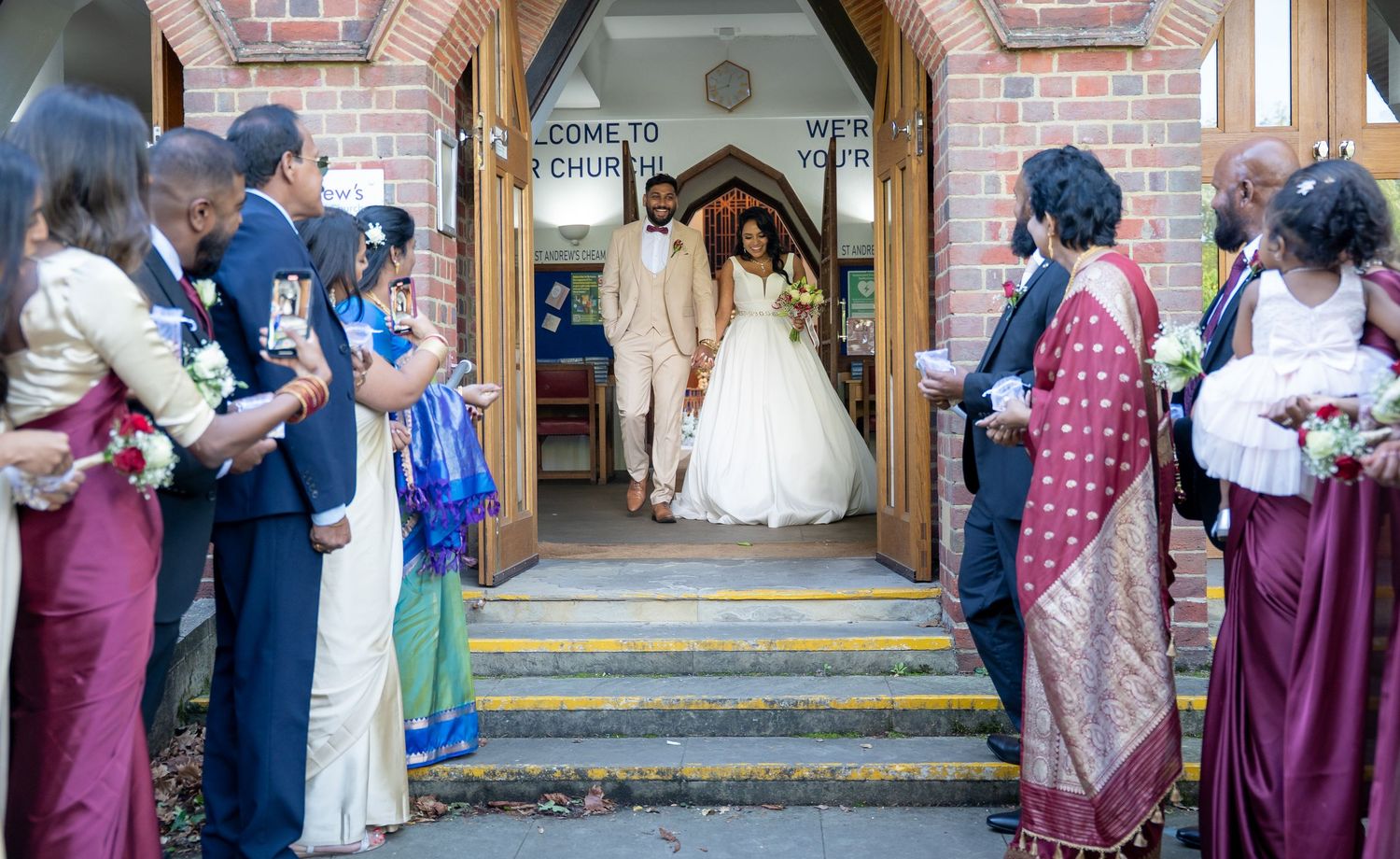 Newlywed couple exits church entrance as guests in traditional attire line steps to celebrate their union.