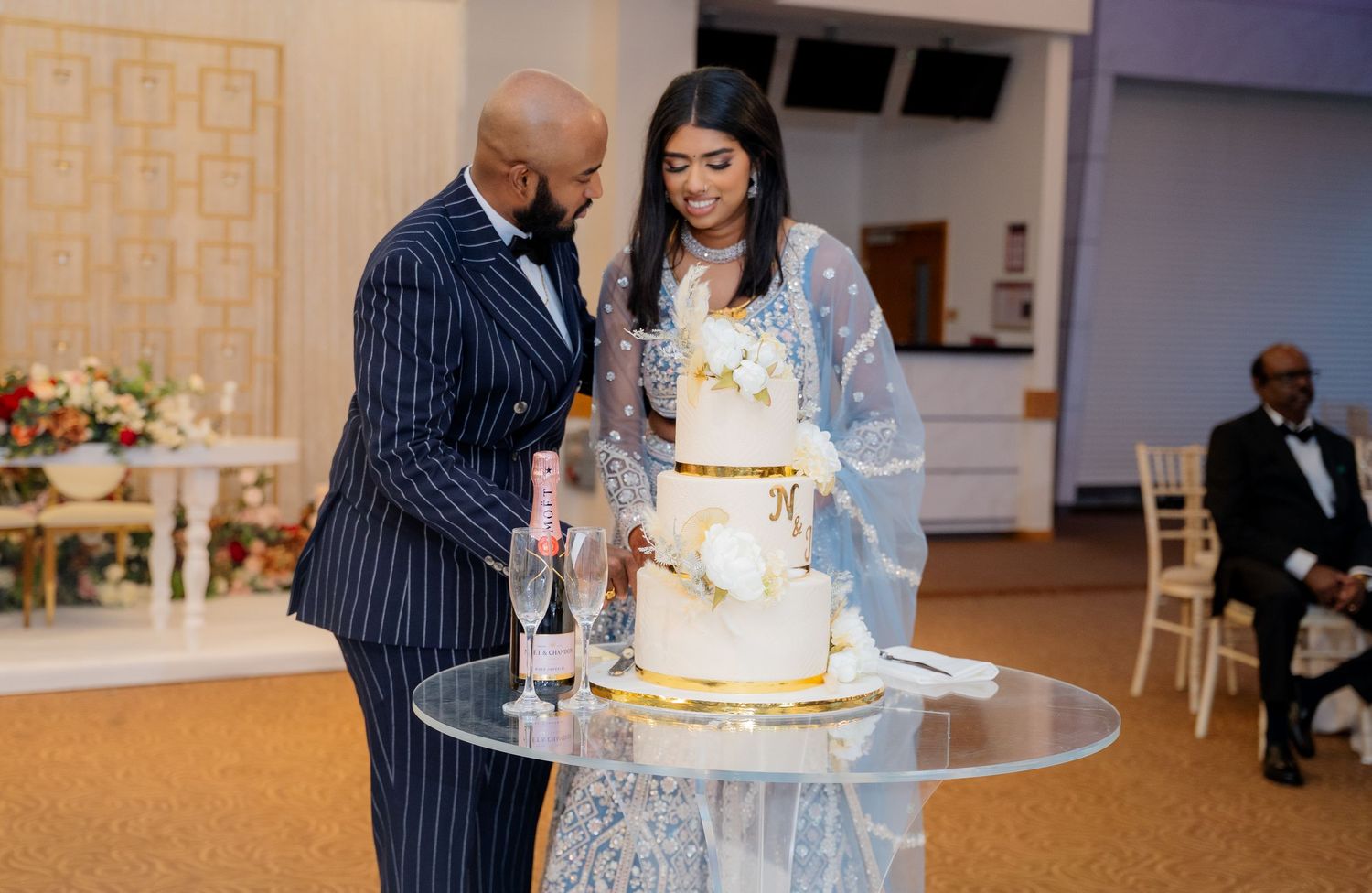 Bride and groom lean in close while cutting elegant white wedding cake at reception.