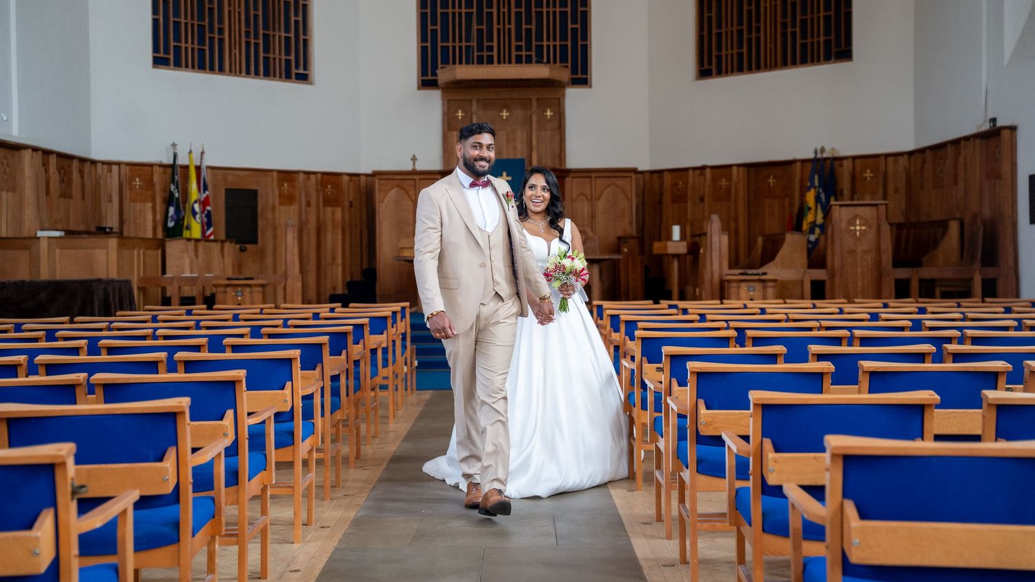 Bride and groom posing together in the center aisle of a church with blue pews.