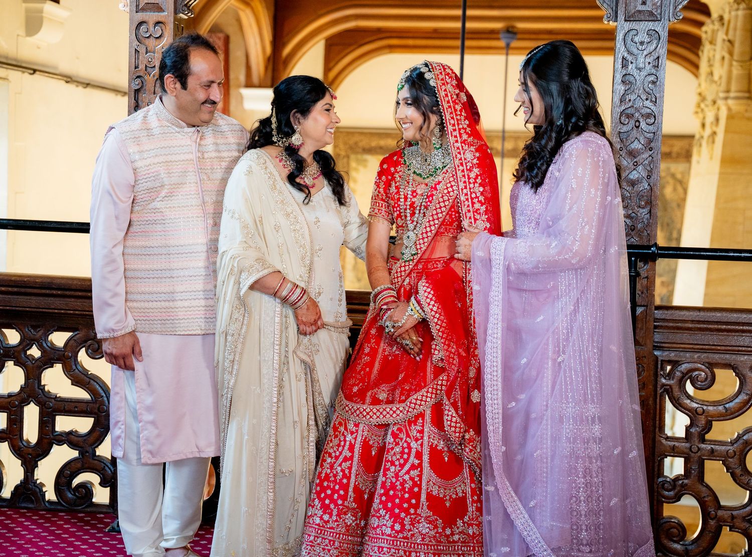 Indian bride in red lehenga with family in ornate wooden wedding venue.