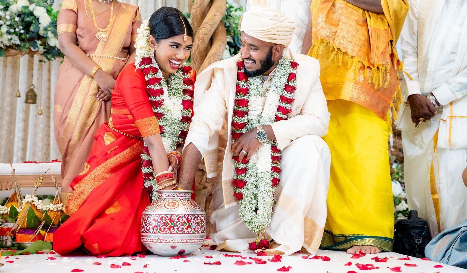 Indian bride in red saree and groom in cream sherwani exchange garlands during traditional Hindu wedding ceremony.