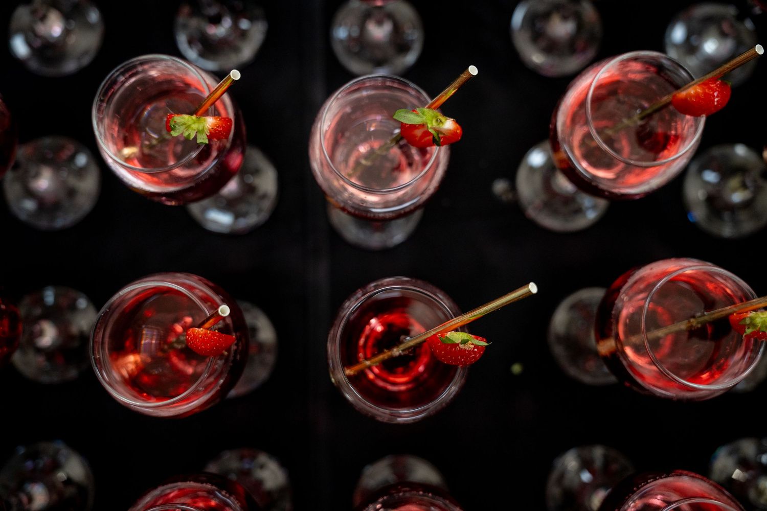 Top-down view of red berry cocktails garnished with strawberries on a dark background.