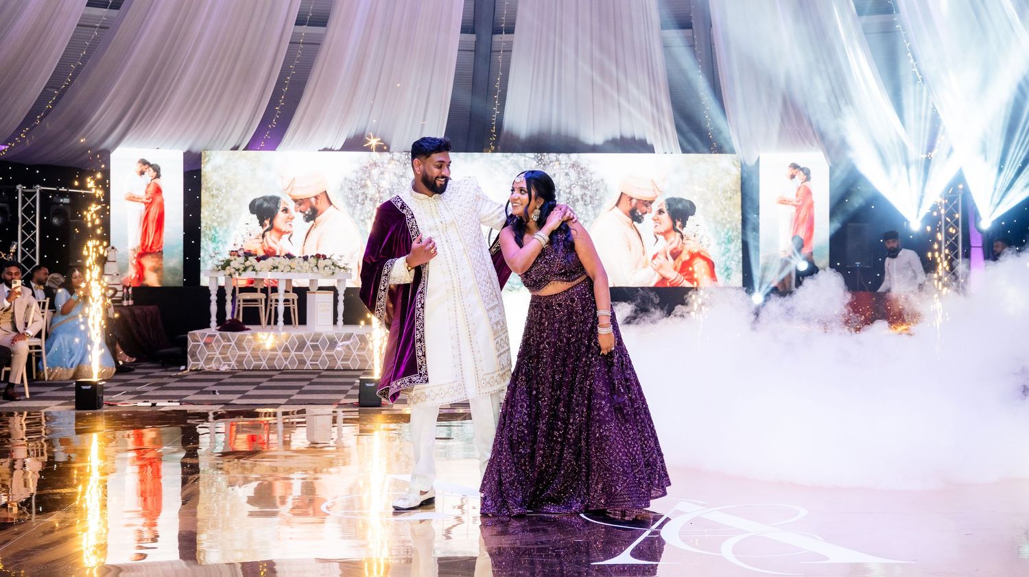 Indian bride and groom making grand entrance onto foggy dance floor at elegant wedding reception.