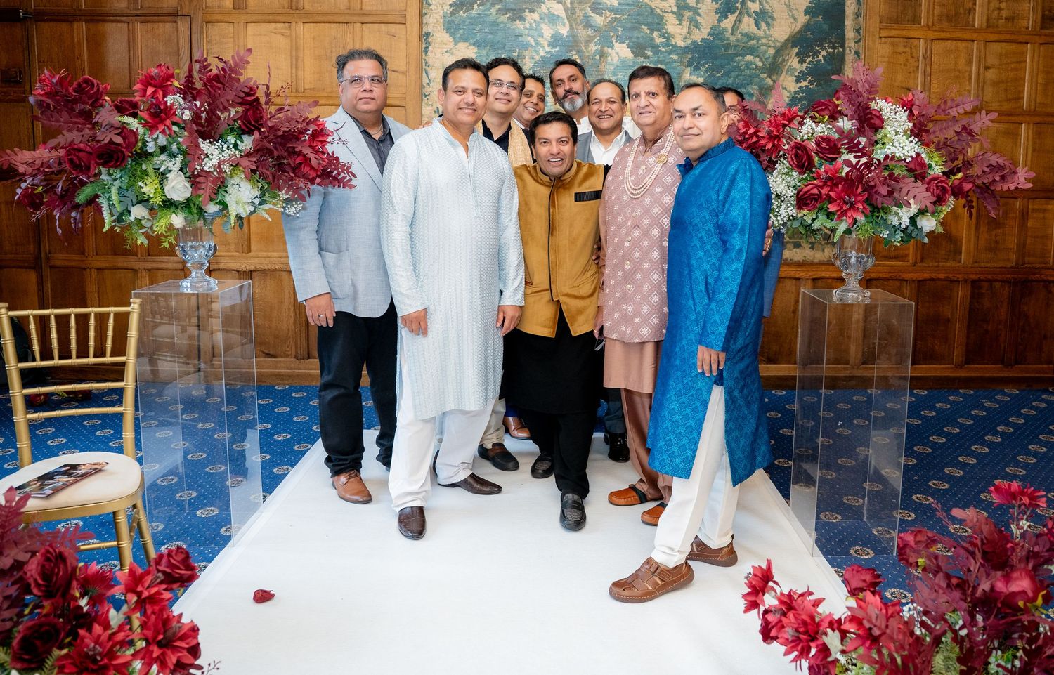 Group of men in traditional South Asian wedding outfits posing together at a decorated wedding venue.