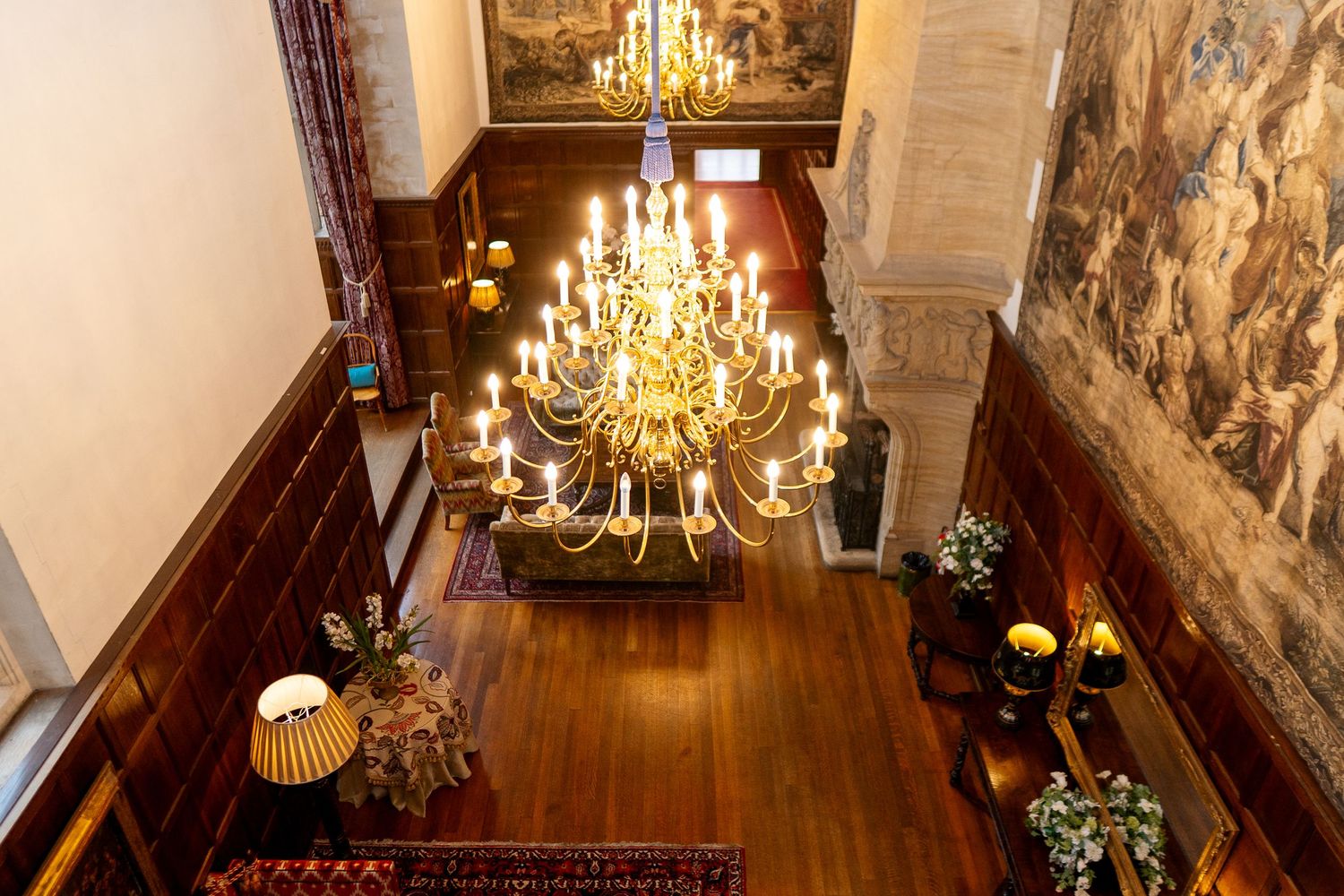 Aerial view of an elegant hotel lobby featuring a grand gold chandelier, hardwood floors, and ornate wall murals.
