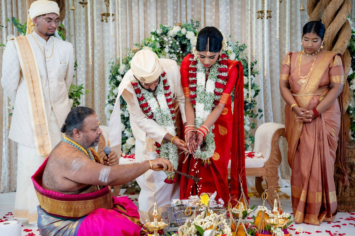 Hindu wedding couple performing sacred rituals at mandap with priest and family members present.