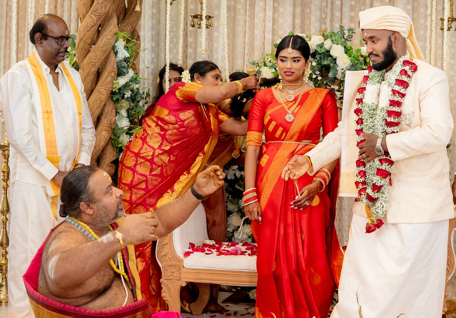 Traditional South Indian wedding ceremony with bride in red saree and groom in white sherwani exchanging garlands.