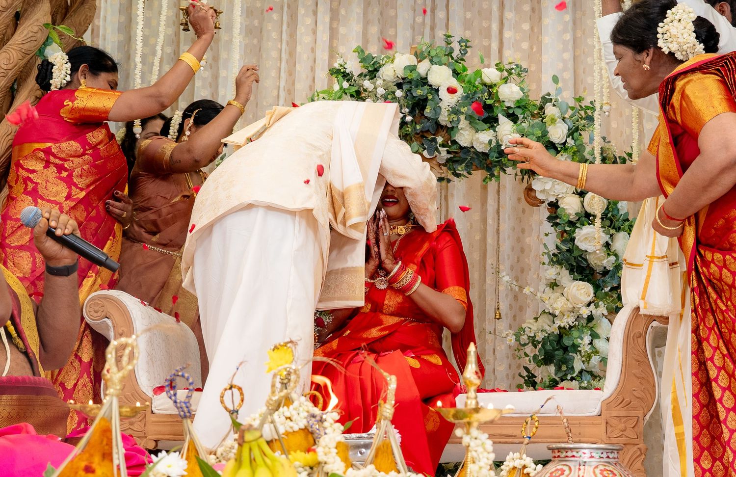 Groom bowing to bride during sacred South Indian wedding ritual with rose petals and floral decorations.