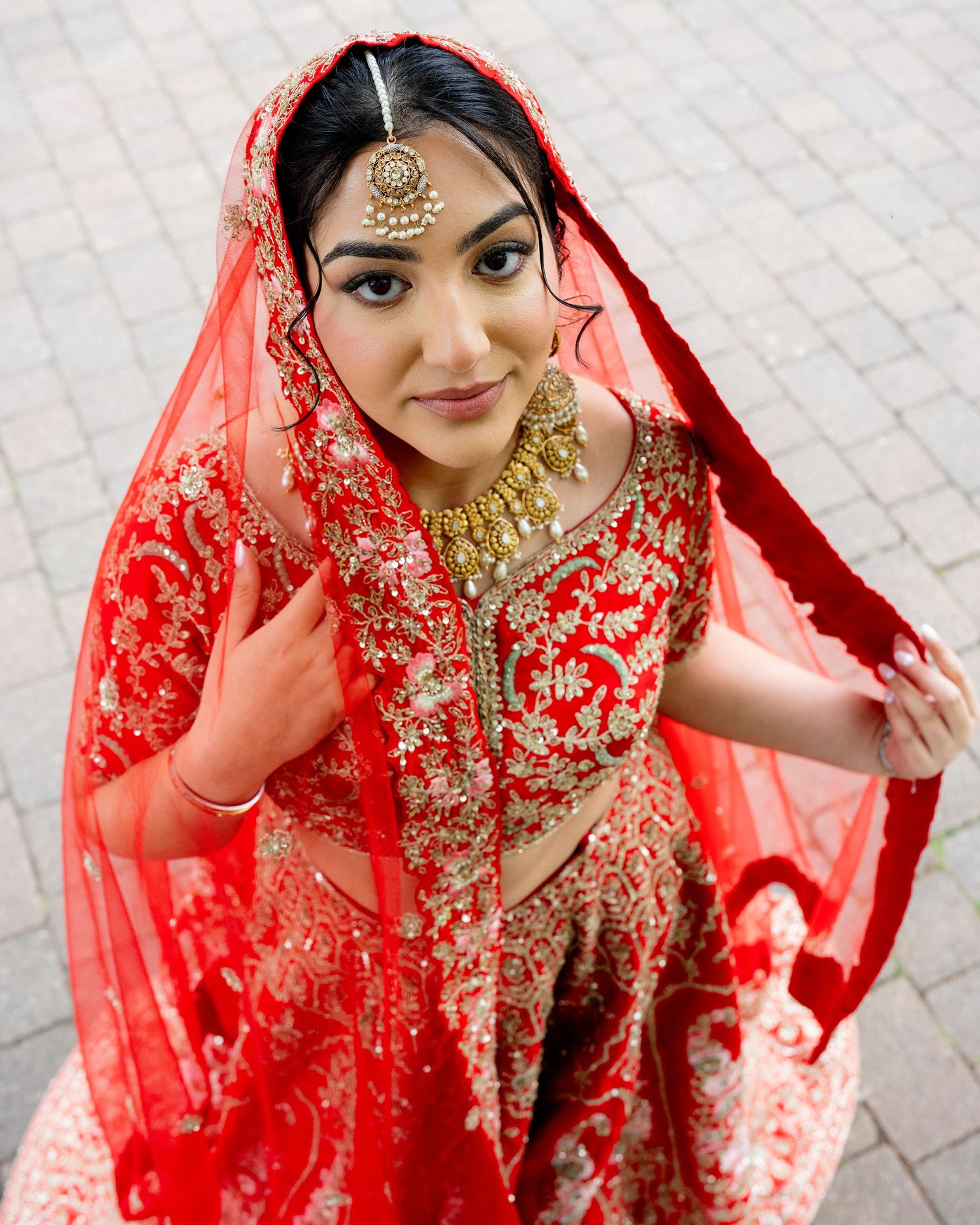 Beautiful Indian bride wearing red bridal lehenga with gold embroidery and traditional gold jewelry.