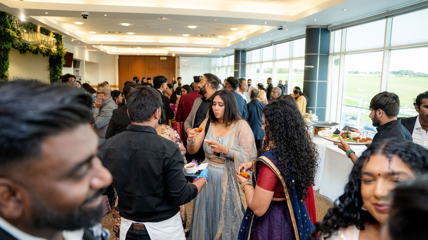 Large crowd of guests in formal and traditional attire mingling at an elegant indoor reception.