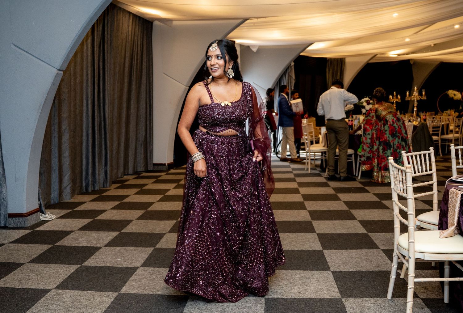 Woman in a stunning purple embroidered lehenga walks confidently across a black and white checkered floor.