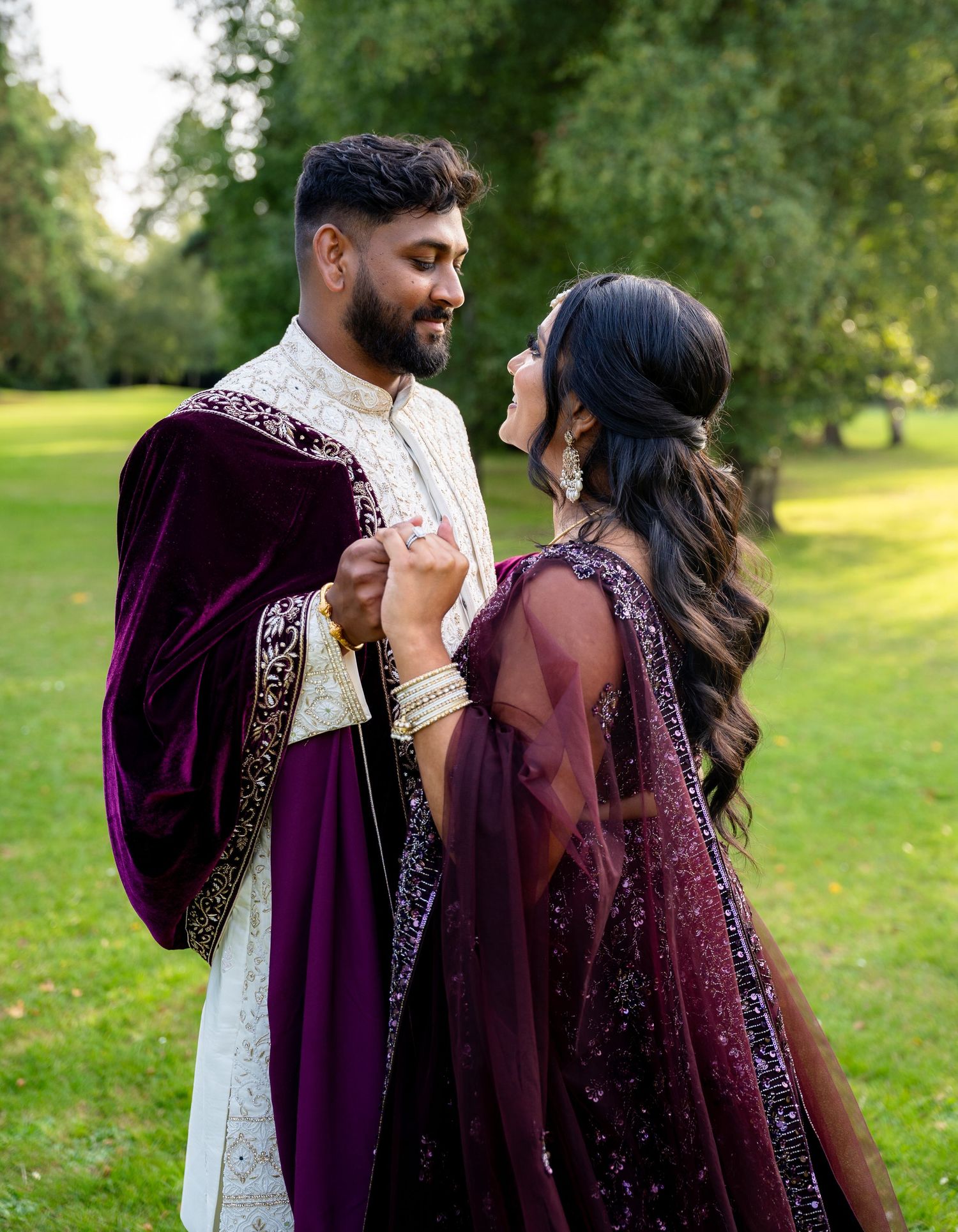 Indian bride and groom sharing intimate moment outdoors, wearing matching purple and white wedding attire.