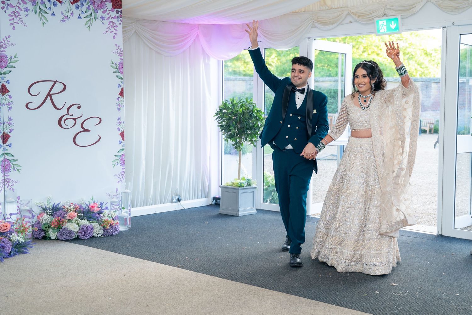 Bride and groom making a grand entrance at their wedding reception in a floral decorated marquee.