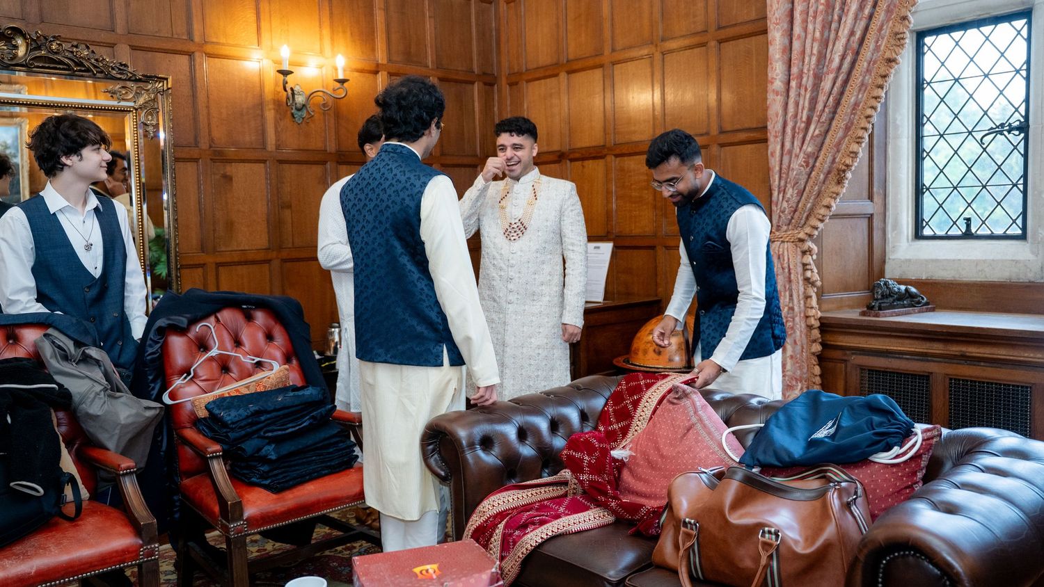 Groom and groomsmen in traditional Indian attire preparing in a wood-paneled room.