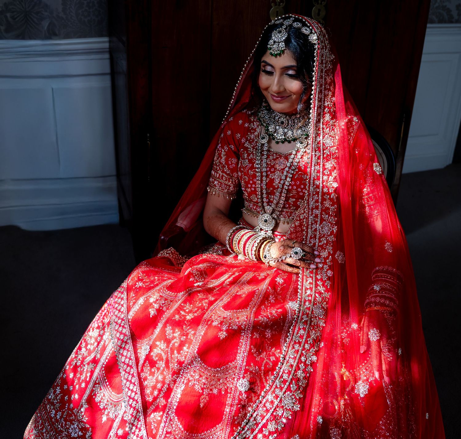 Beautiful Indian bride in red bridal lehenga and dupatta with traditional jewelry smiling.