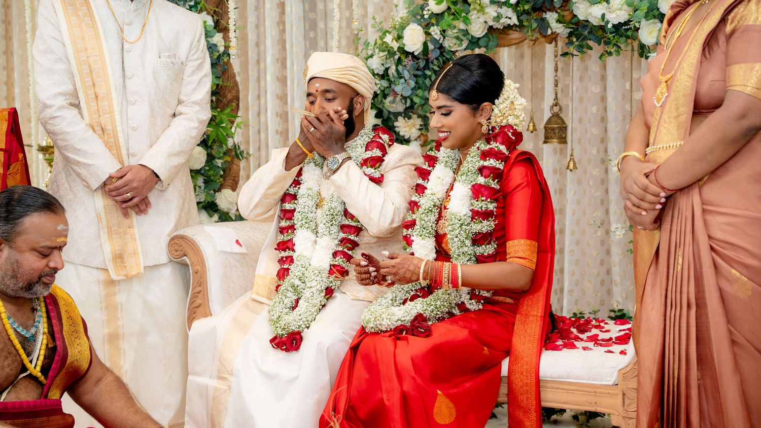 Groom covers mouth emotionally during heartfelt South Indian Hindu wedding ceremony beside bride in red.