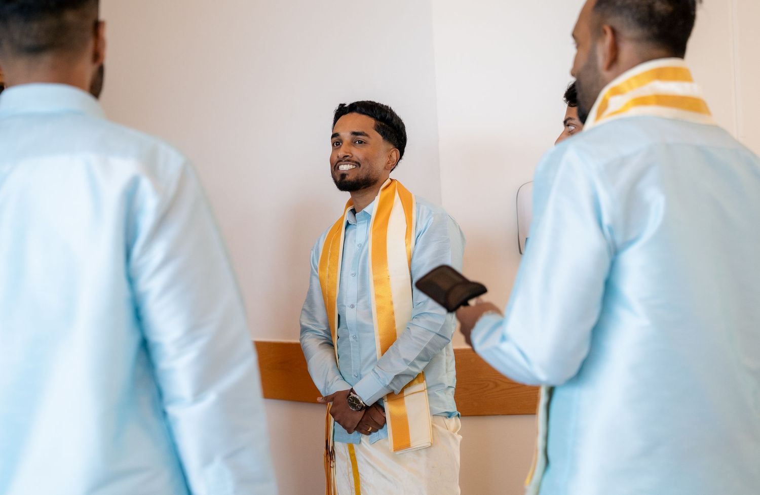 Indian groom in light blue kurta with gold dupatta smiles with groomsmen before wedding.
