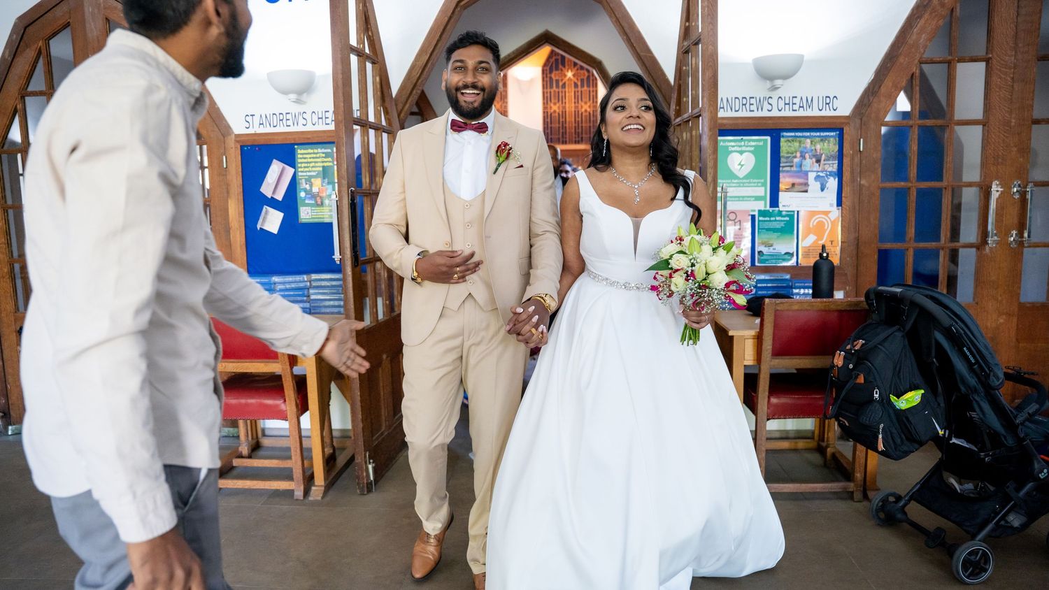 Bride and groom walking down church aisle in wedding attire, bride in white gown holding bouquet.