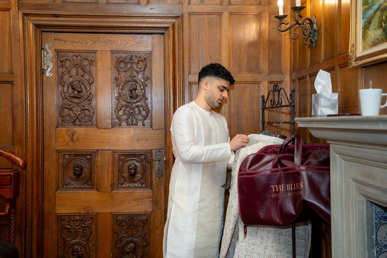 Groom in white traditional Indian kurta preparing for his wedding ceremony in an elegant room.