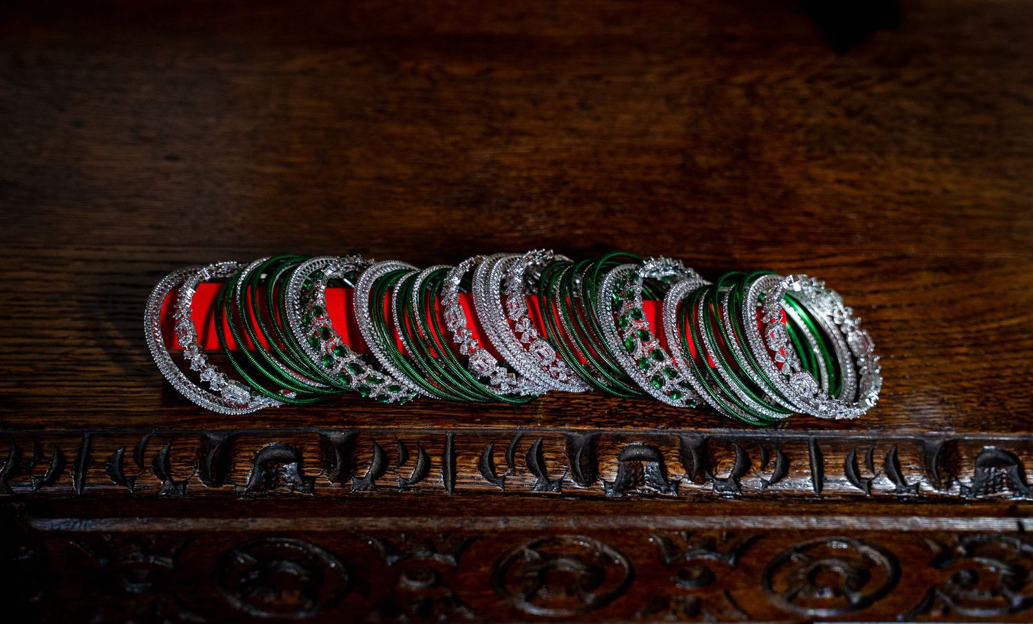 Stack of colorful red and green Indian wedding bangles displayed on carved wooden surface.