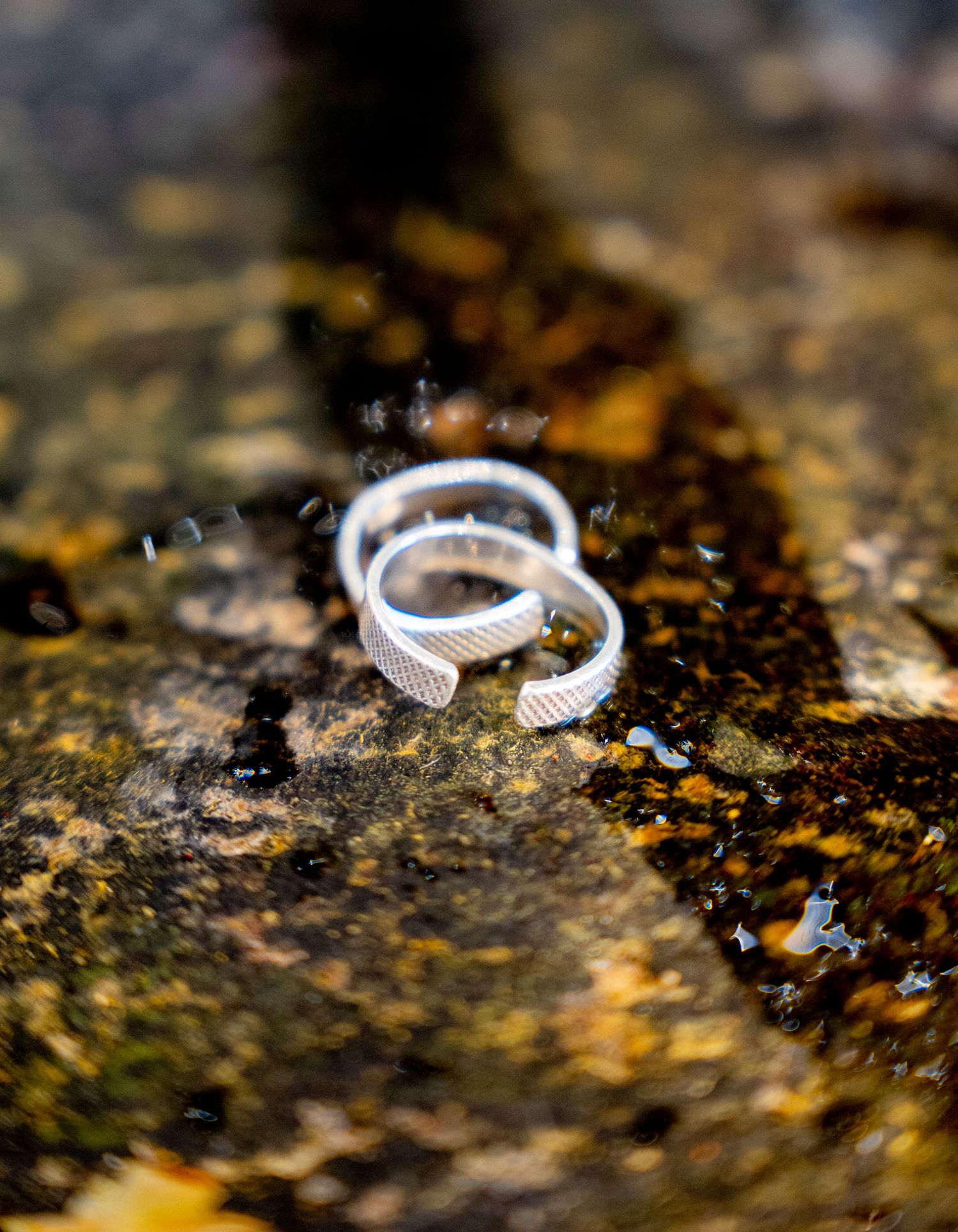 Two silver textured wedding bands placed together on a weathered mossy stone surface.