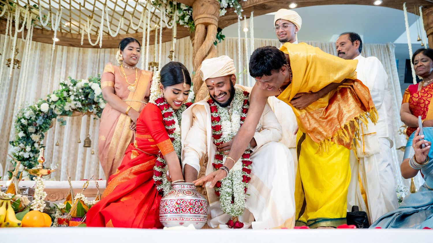 Family members gather around the bride and groom during an auspicious pot ceremony at a Hindu wedding.