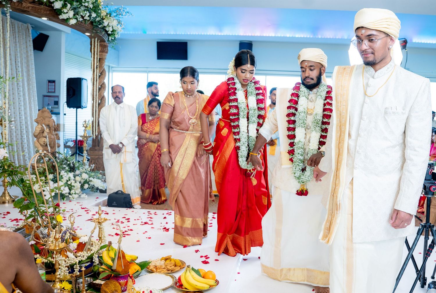 Bride and groom walk together during traditional Hindu wedding ceremony with rose petal aisle.