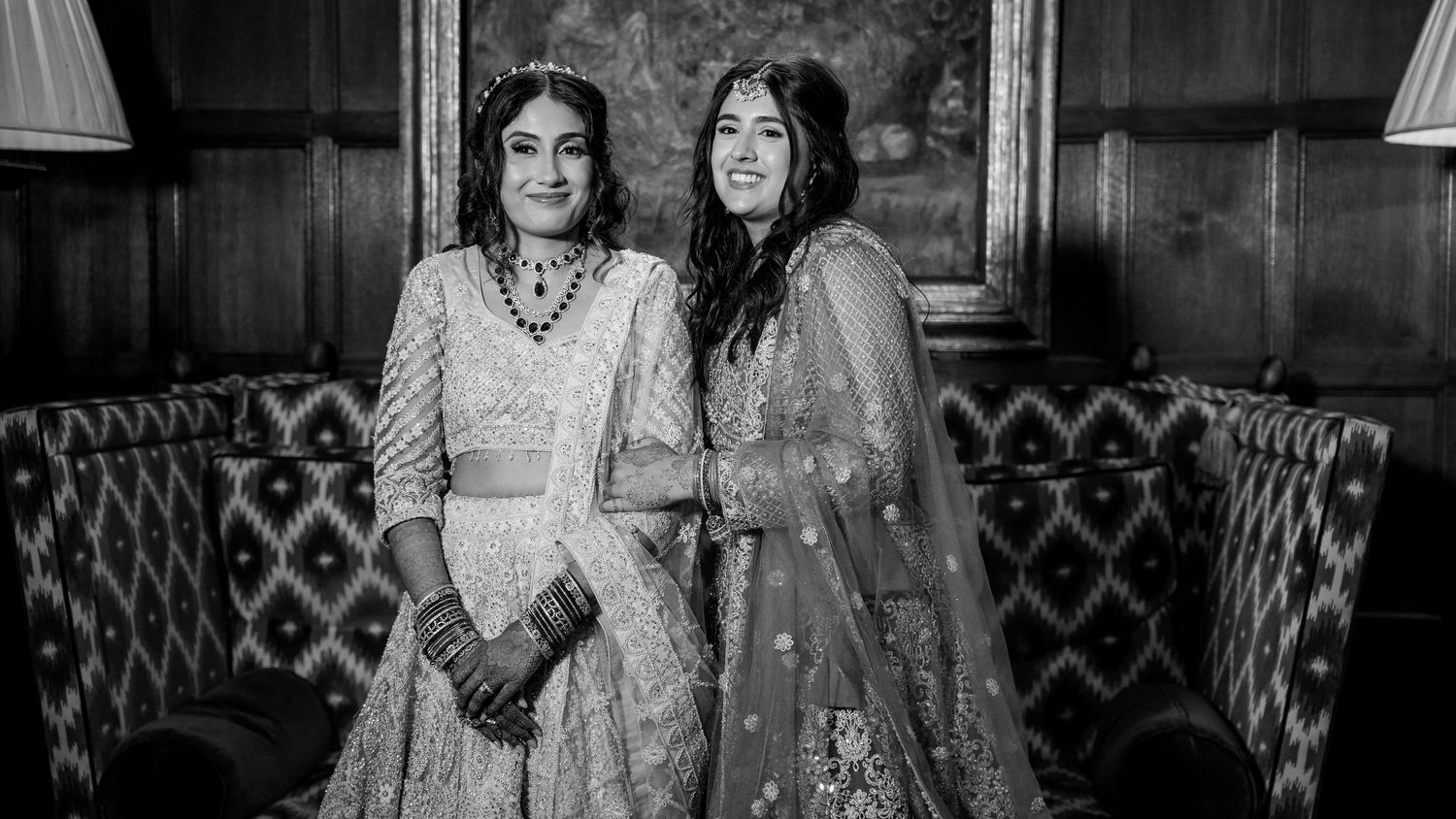 Black and white photo of two women in traditional Indian attire smiling together at a wedding celebration.