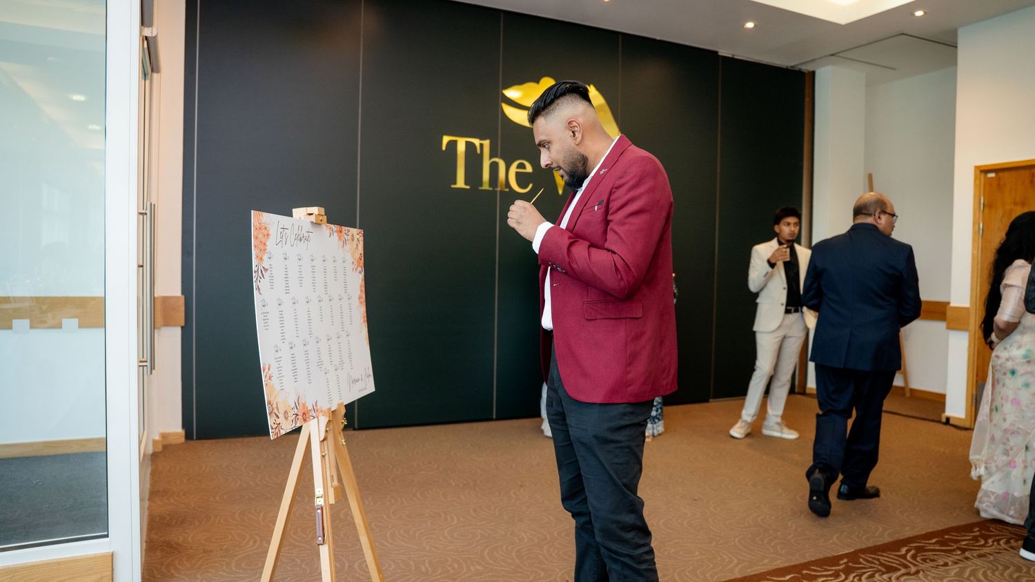 Man in red blazer reviewing seating chart on easel at The Views formal event venue.