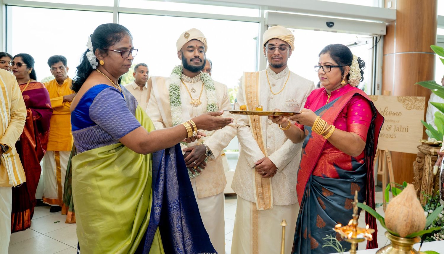 Group of people in traditional Indian attire exchanging gifts during a cultural ceremony with priest present.