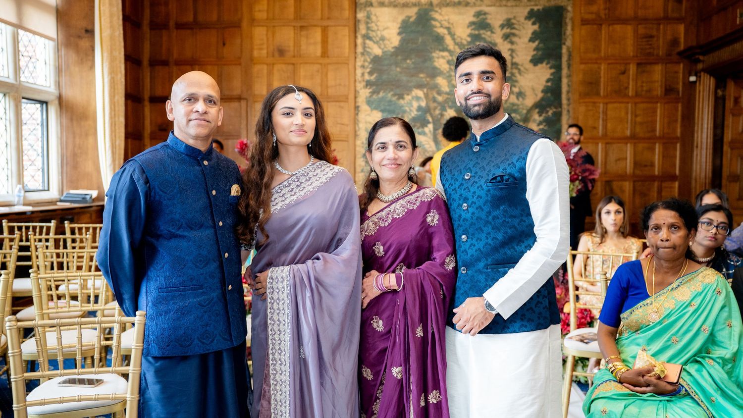 Four people in traditional Indian attire posing together at an elegant indoor wedding ceremony venue.