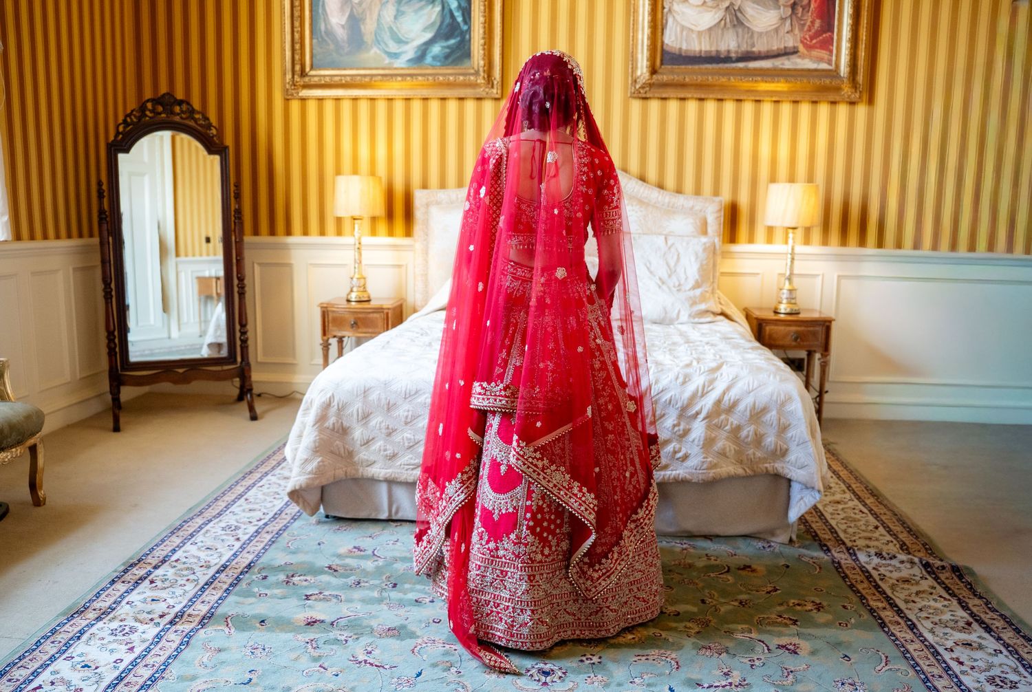 Back view of Indian bride in red embroidered lehenga with dupatta in elegant bridal suite.