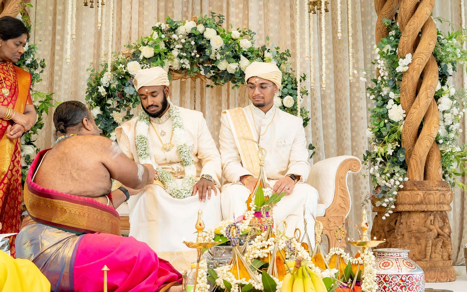 Hindu wedding ceremony with two grooms in white as a priest performs traditional rituals.
