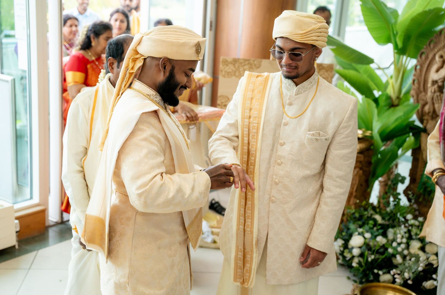 Two men in cream and gold sherwanis sharing a warm moment together during a traditional Hindu wedding celebration.
