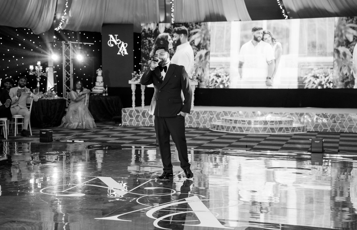 Black and white photo of MC performing speech on dance floor at elegant Indian wedding reception.